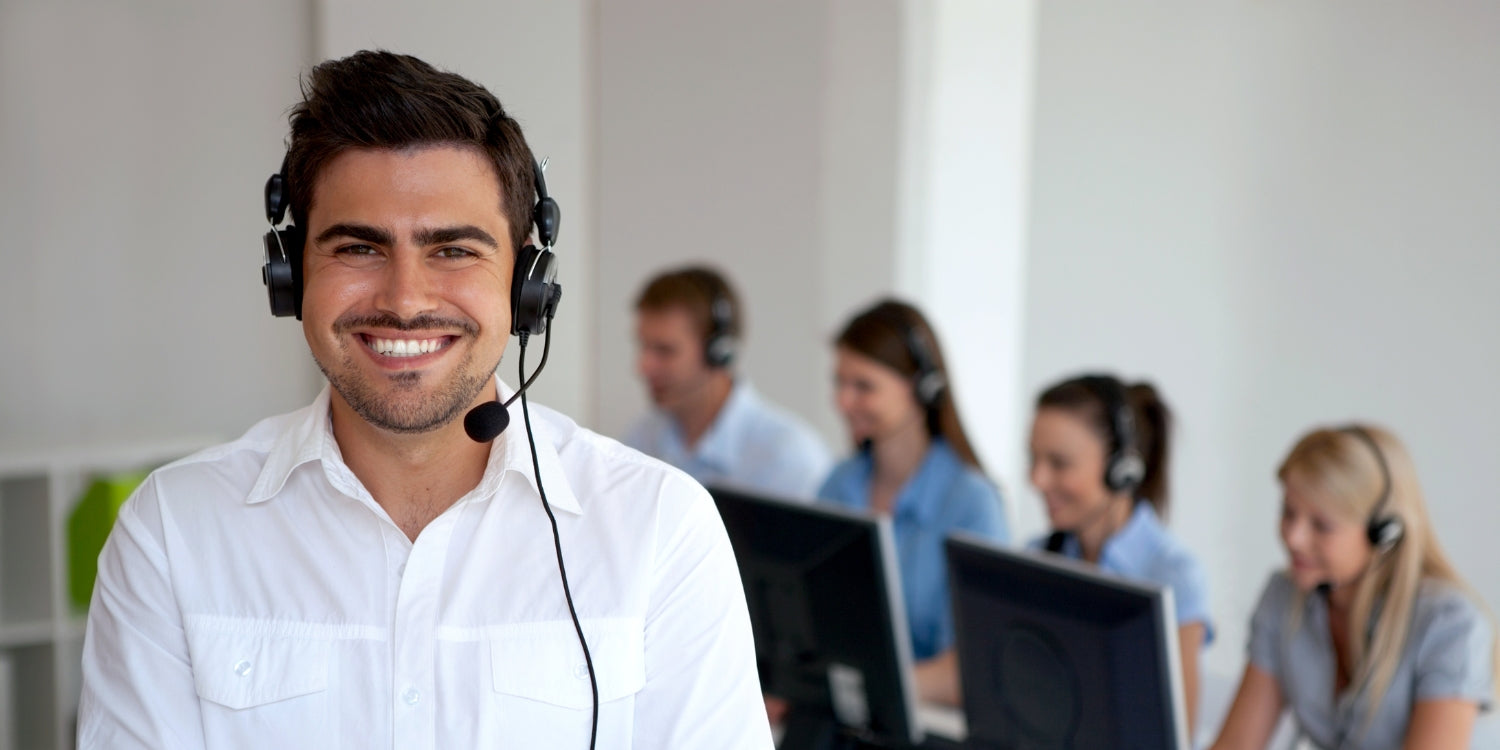 Kundenservice Mitarbeiter mit Headset auf dem Kopf und arbeitende Mitarbeiter dahinter